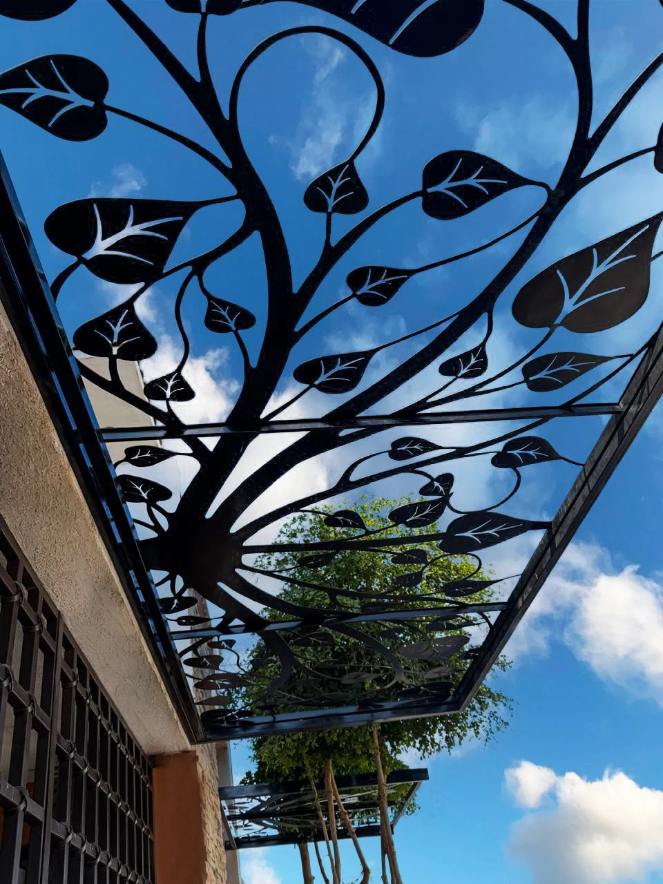 Techo de celosía metálica con diseño de hojas visto desde abajo contra el cielo